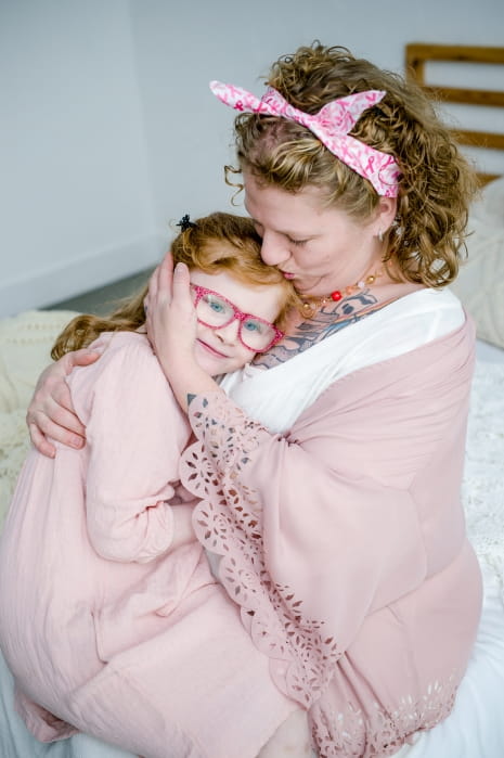 woman wearing pink holding child dressed in pink, kissing child's forehead