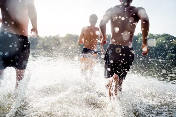 camera view behind three young teenage boys running splashing in lake water