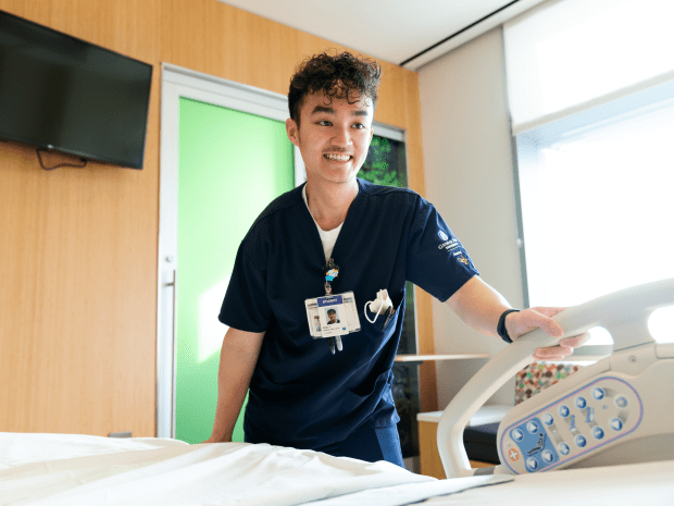 Photo of Peter Tran in a hospital room, with a hand on the side of the bed