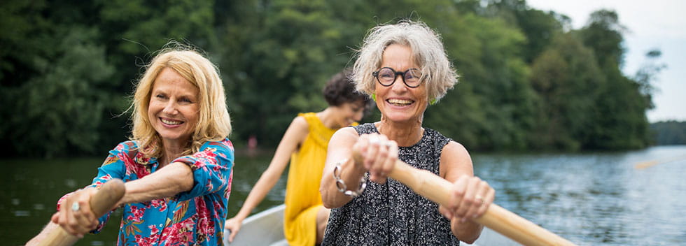 Smiling female friends rowing boat in lake