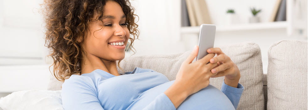 Pregnant woman, smiling and reading on device