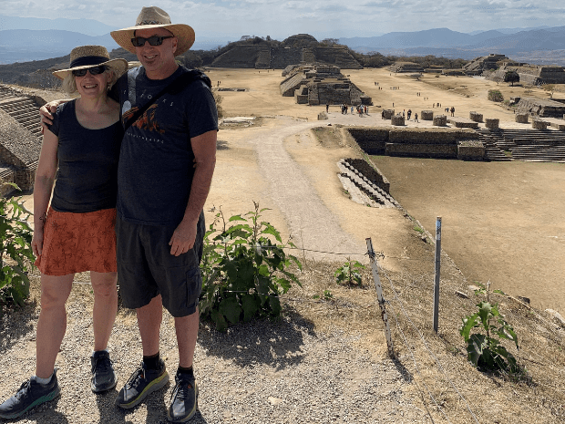 Wendy Berger and man posing on a cliff above ruins on a vacation trip