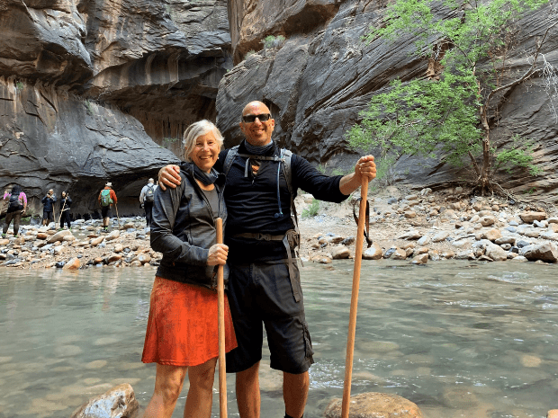 Wendy Berger posing with man with walking sticks in a lake, with large rock formations in the background