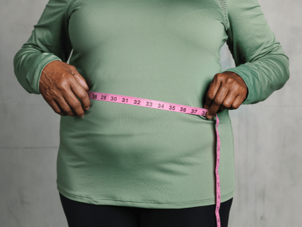 Photo of individual wearing green shirt holding pink measuring tape across their stomach