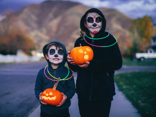Children trick or treating wearing costumes and glow sticks while holding pumpkins