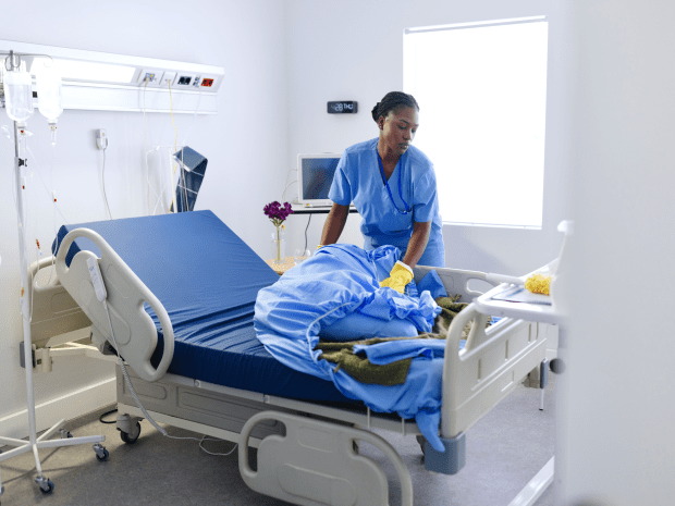 Nurse wearing medical scrubs in a hospital setting changing the bedsheets