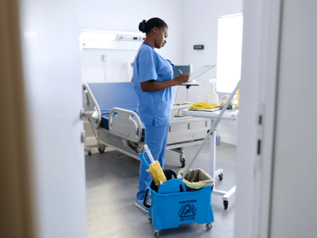 Nurse wearing medical scrubs in a hospital setting taking notes with cleaning supplies near her